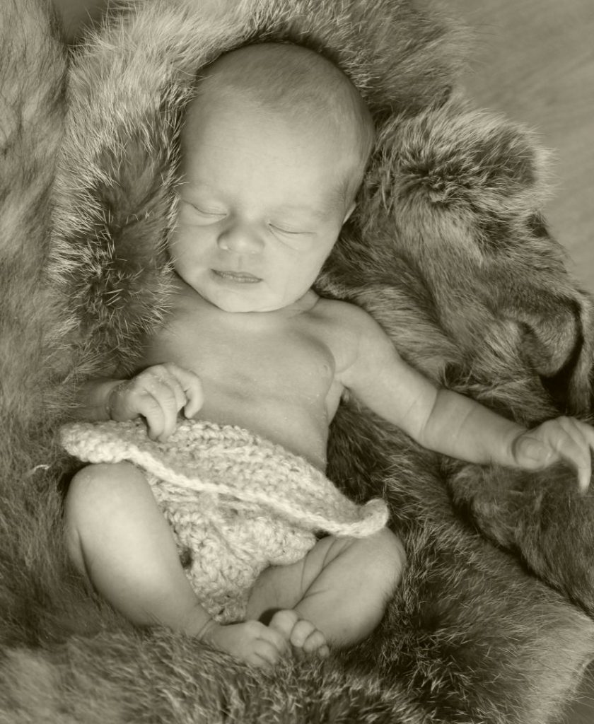 Ein besonders entzückendes Baby liegt (nur mit einer naturfarbenen, gehäkelten Windel bekleidet) in einem Fell