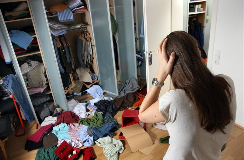 Frau steht entsetzt vor dem ausgeräumten Kleiderschrank. Die Sachen liegen zum Teil auf dem Boden. Ein Einbruch.