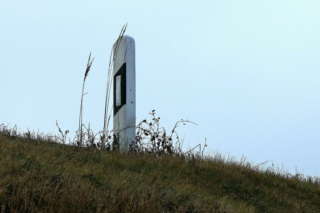 Ein Leitpfosten (unbeschädigt) steht am Straßenrand - der angrenzende Hang ist mit Gras bewachsen.