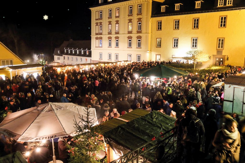 Das beleuchtete Schloss Wittgenstein und eine Menge von über 100 winterlich gekleideten Besuchern. Viele Buden sind auf dem Platz aufgebaut.