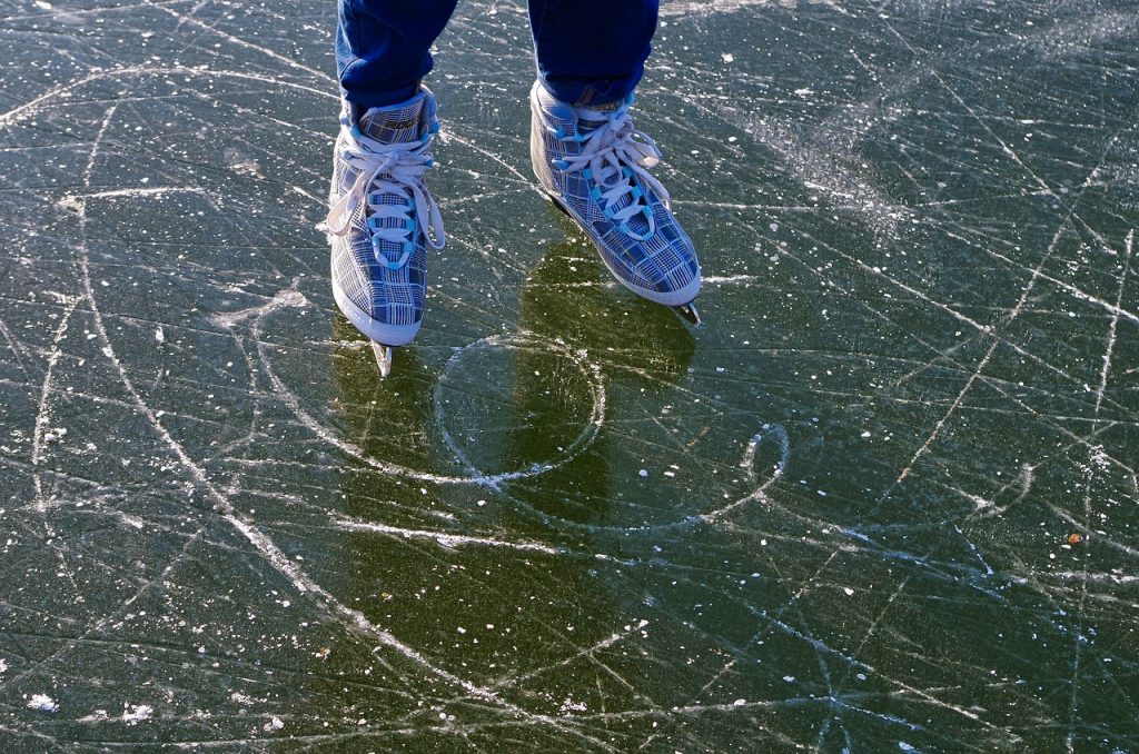 Ein Bildausschnitt: eine Eisfläche und zwei Kinderfüße in Schlittschuhen. Ein Stückchen von den Beinen ist zu sehen.