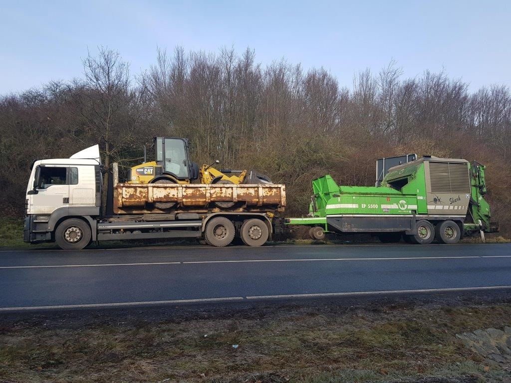 Zwei Lkw stehen am Straßenrand. Einer hat einen Bagger geladen. Dieser wurde nicht korrekt gesichert.