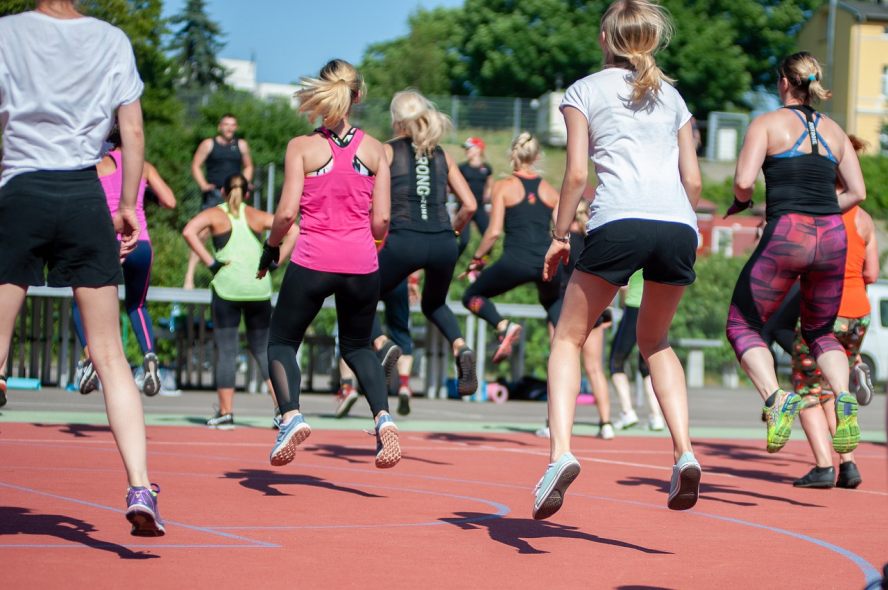 Hüpfende Frauen in einer Gruppe in Sportkleidung auf einem Sportplatz im Freien.