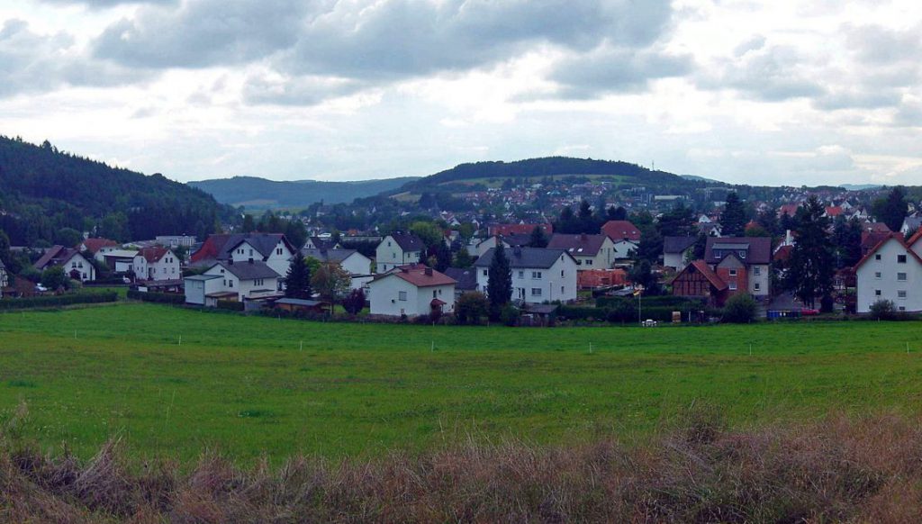 Gladenbach - Häuser von Nordosten aus. Vorn: Wiese. Hinten: Berge und Himmel.