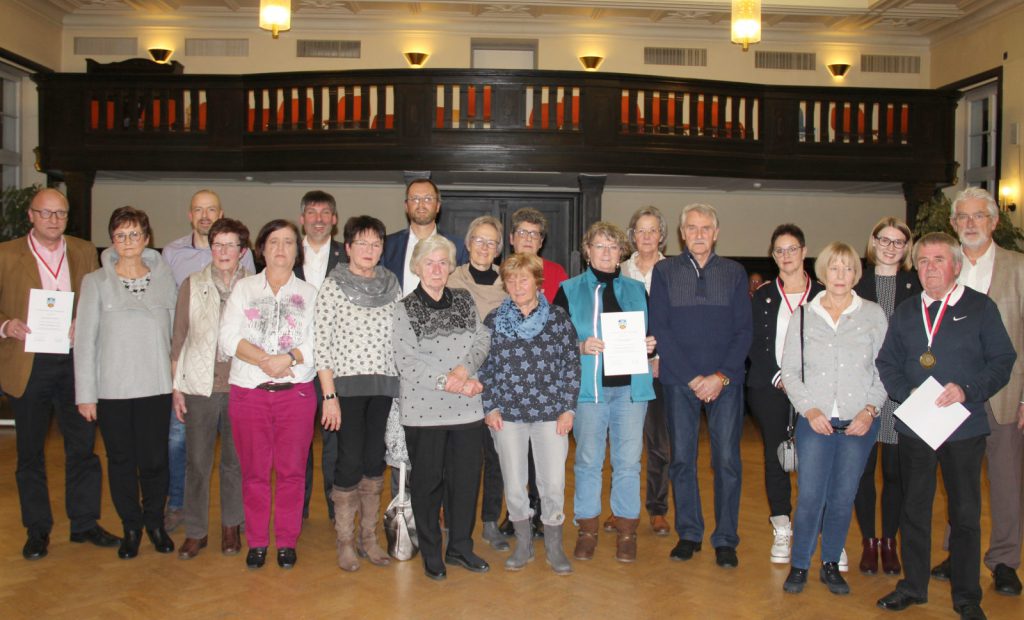 In der Aula vor der Empore stehen die Ehrenamtspreisträger mit Bürgermeister und Stadtverordnetenvorsteher zum Gruppenbild.