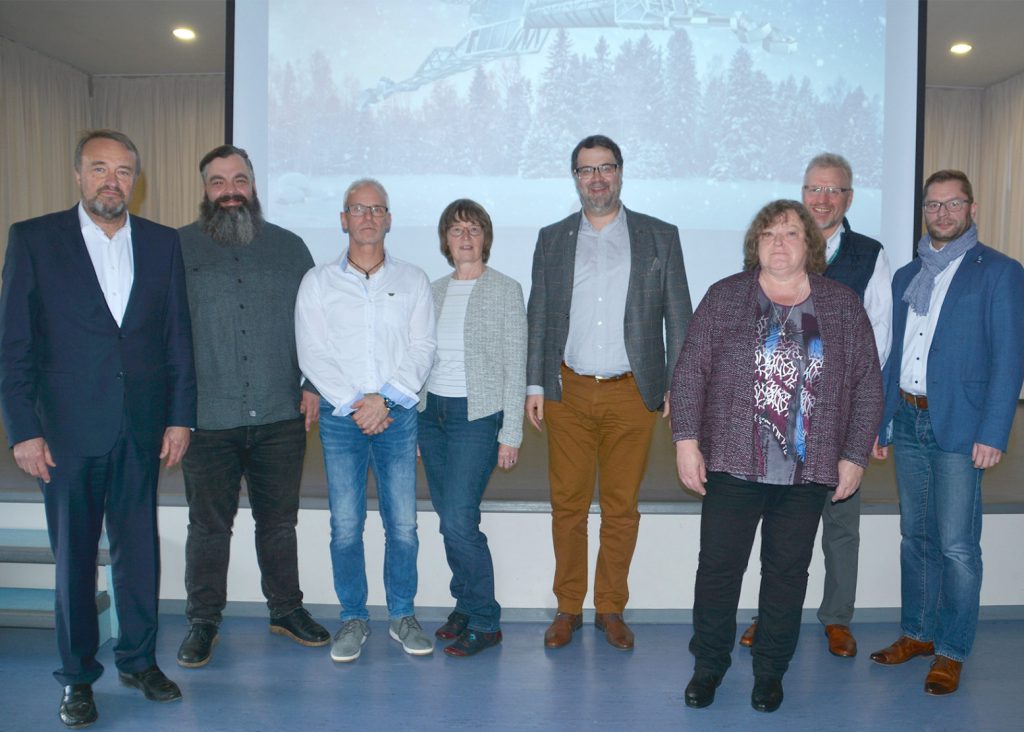 Die Geehrten stellen sich zum Gruppenfoto. Im Hintergrund ein winterliches Bild auf Leinwand.