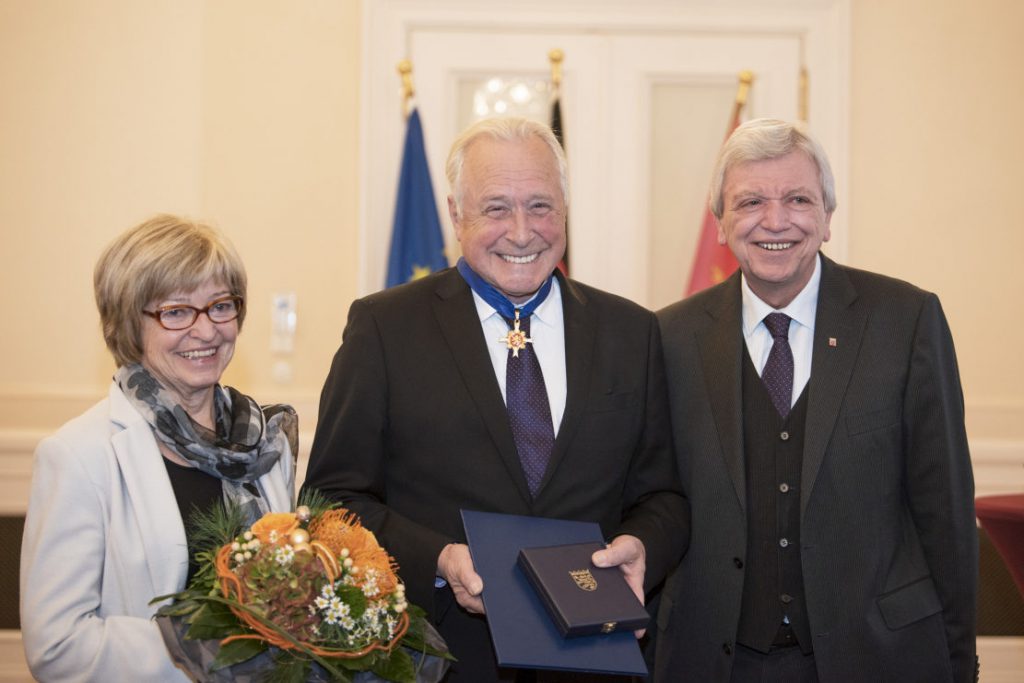 Frau Fischbach mit Blumenstrauß, Robert Fischbach in der Mitte mit dem neuen Verdienstorden um den Hals und rechts Minister Bouffier. Alle strahlen.
