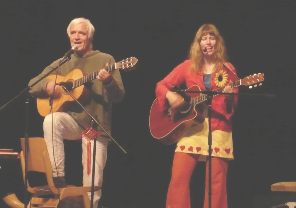 Ein Mann und eine Frau - beide mit Gitarre im Anschlag - singen vor schwarzem Hintergrund.