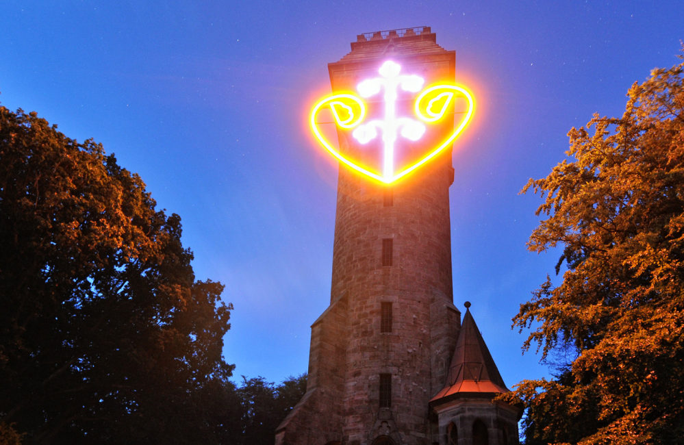 Kaiser-Wilhelm-Turm bei Nacht mit leuchtendem Herzen. Bäume rechts und links.
