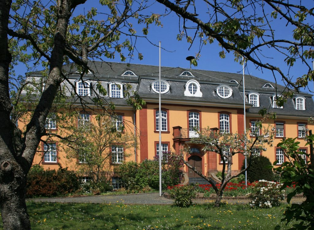 Das Landratsamt (Front) mit Erker und Gauben. In Biedenkopf. Im Frühling. Blühende Bäume im Vordergrund.