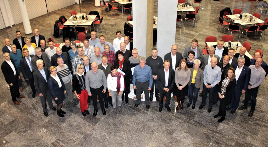Gruppenfoto mit Arbeitsjubilaren, Rentnern und Vorstandsmitgliedern im Roth-Atrium. Im Hintergrund gedeckte Tische.