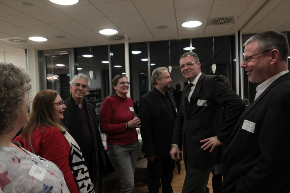 In lockerer Runde stehen sieben Besucherinnen und Besucher im Foyer zusammen bei einem Getränk.