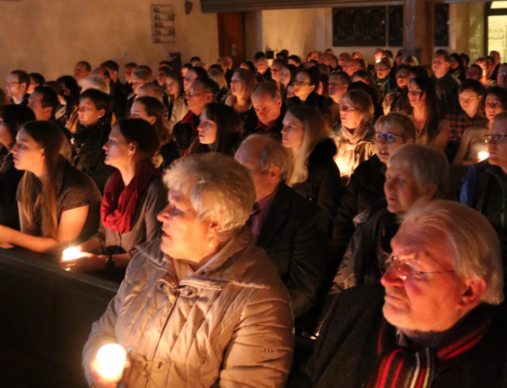 Zuschauer jeden Alters in der vollbesetzten Kirche. Die Atmosphäre ist vom Licht her sehr stimmungsvoll.