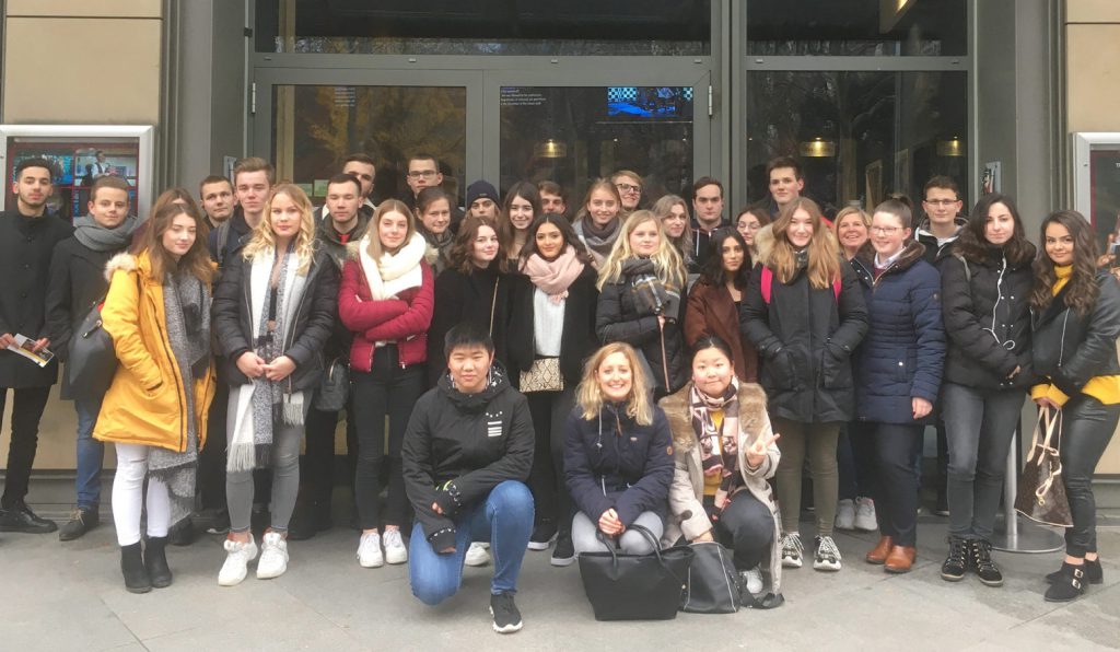 Etwa 40 Schülerinnen und Schüler stellen sich zum Gruppenfoto vor dem Theatereingang. Drei hocken davor.