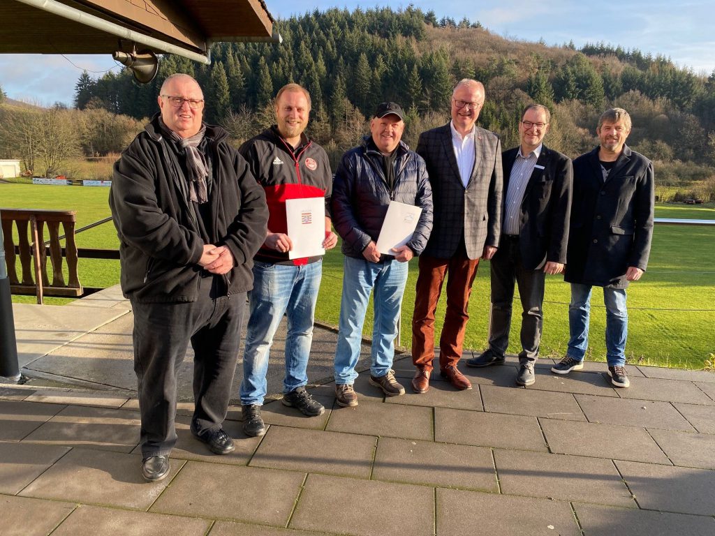 Fünf Fußballvereinsmitglieder mit Finanzminister Schäfer stehen in Reih und Glied und freuen sich über das Geld.