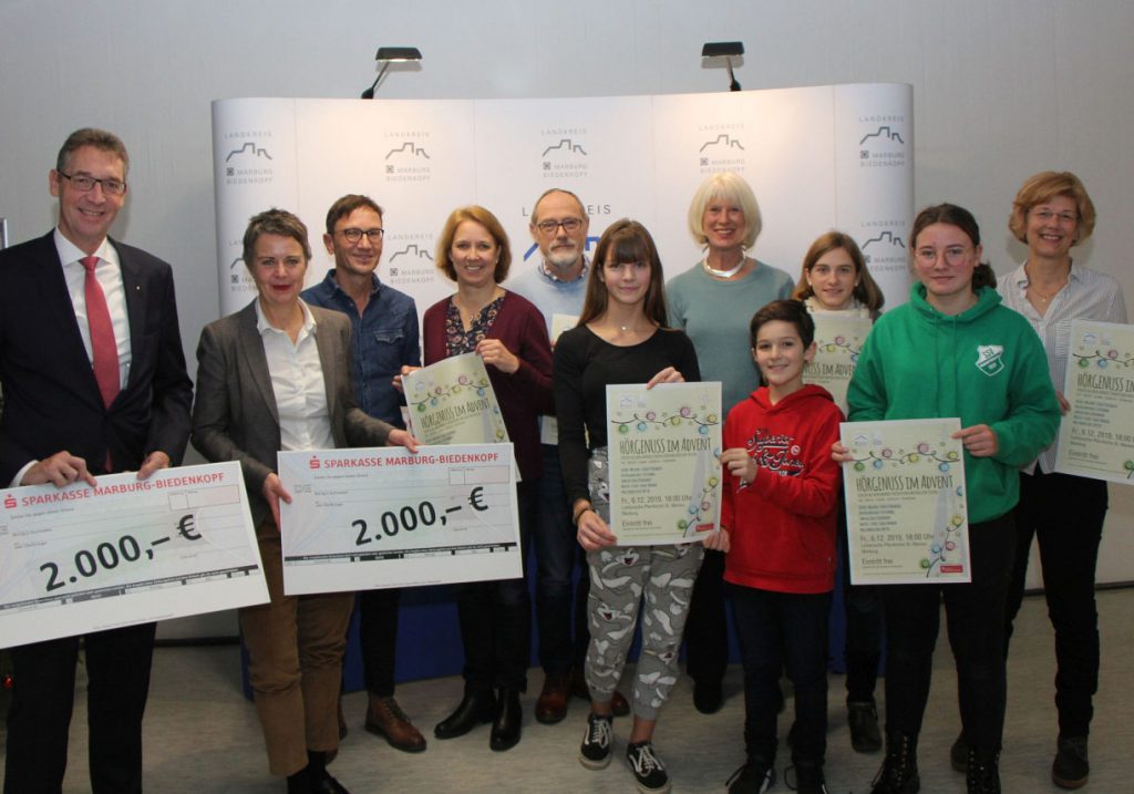 Große und kleine Menschen mit symbolischen Schecks stellen sich lächelnd zum Gruppenfoto vor eine Tafel mit Landkreis-Symbolen.