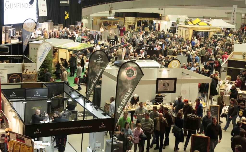 Überblick in die Messehalle. Stände und viele Besucher. Überall Werbeaufsteller.