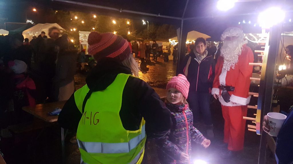 Ein Kind am Glücksrad, daneben weitere Weihnachtsmarktbesucher und der Nikolaus persönlich.