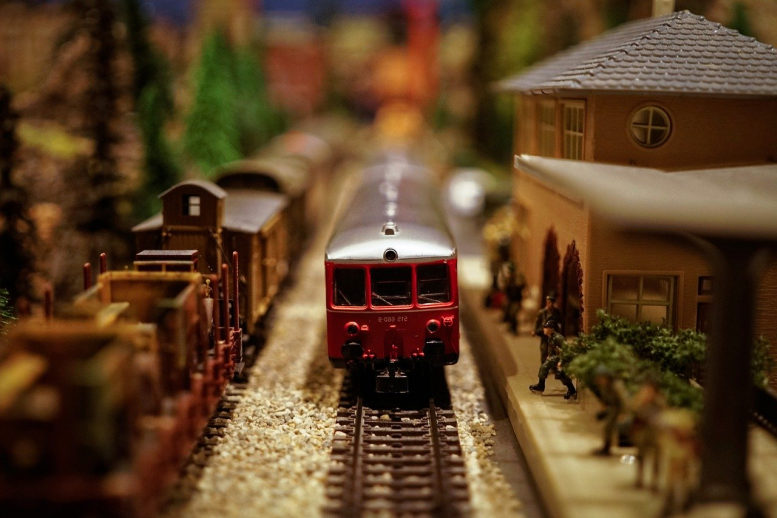 Eine Modellbahnanlage (Ausschnitt). Eine rote Lok aus den 80ern in einem Bahnhof, daneben Güterwaggons, alles im Miniformat.
