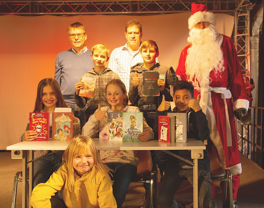Die fröhlichen Sieger des Vorlesewettbewerbs (dre Mädchen und drei Jungs) mit zwei Lehrern und dem Nikolaus beim Gruppenfoto