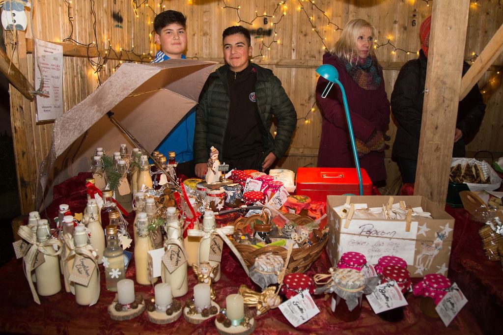Zwei Jungs stehen vor einem Stand mit liebevoll dekorierten Geschenkartikeln - Flaschen, Kerzen und Konfitüren.