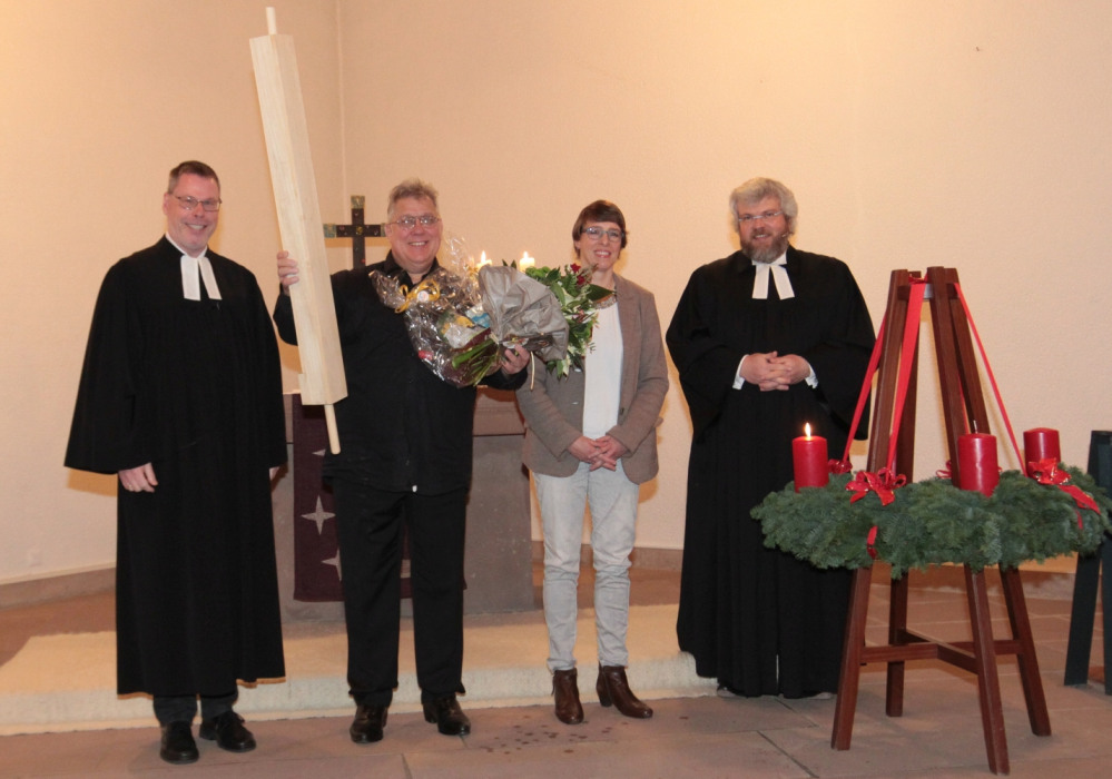 Dekanatskantor Burghardt Zitzmann hält sein Geschenk: eine überdimensionale Orgelpfeife aus Holz sowie Blumen im Arm. Mit ihm freuen sich Andreas Friedrich und Pfarrer Axel Henß (beide im Talar) sowie Propsteikantorin Petra Denker.