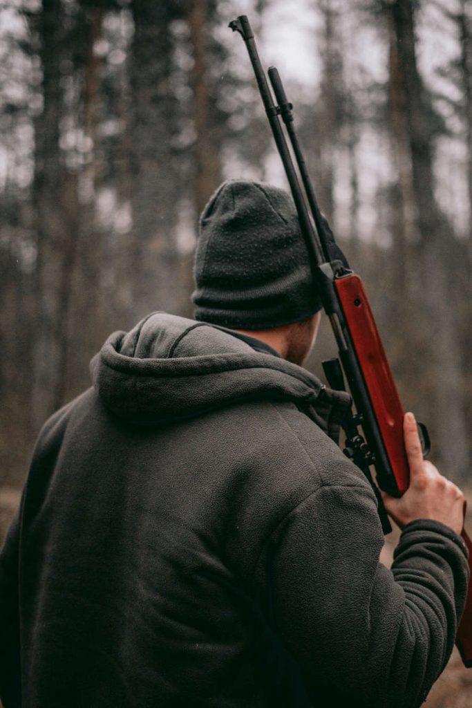 Jäger, von hinten zu sehen, mit geschultertem Gewehr im Wald.