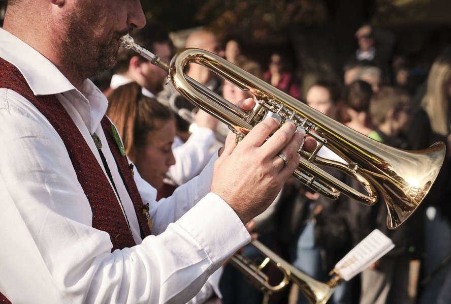 Drei Trompetenbläser, nur angedeutet zu sehen. Leute im Hintergrund.