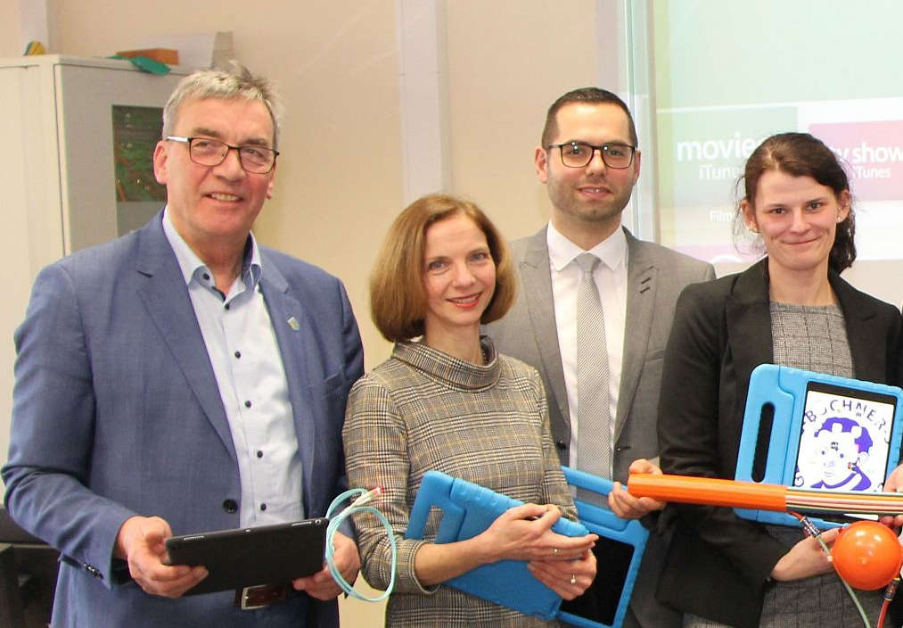 Vier offizielle Vertreter (2 Frauen und w Männer) mit Schüler-Laptops.