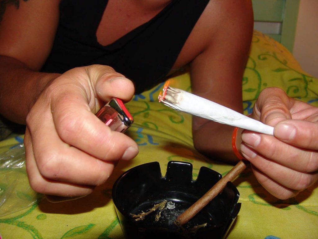 Ein Mann (nur Arme und Oberkörper zu sehen) zündet sich einen Joint an.