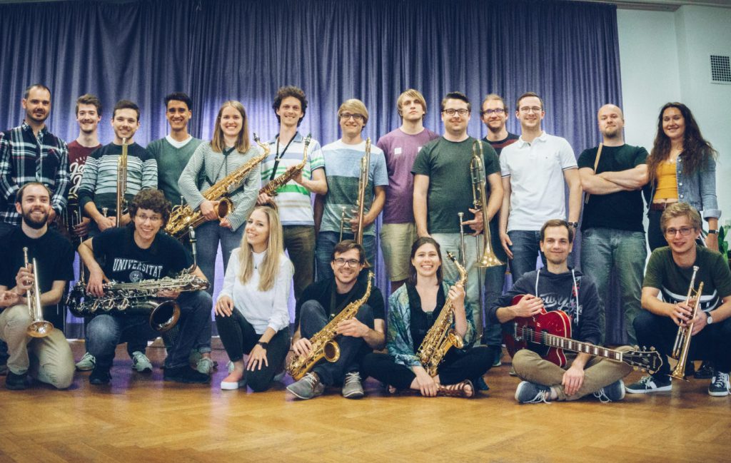 20 Studentinnen und Studenten stellen sich mit ihren Instrumenten - von Posaune bis Saxophon - zum Gruppenfoto. Die vordere Reihe hat sich gehockt.