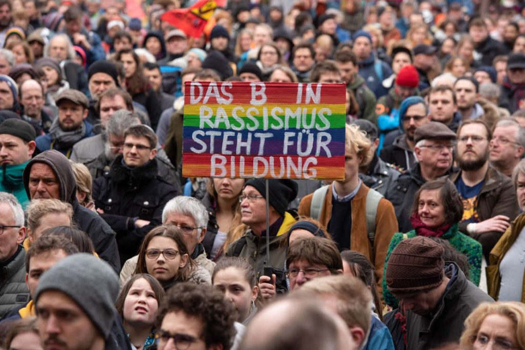 In der Menge der Demonstranten hält einer ein Schild hoch. "Das B in Rassismus steht für Bildung".