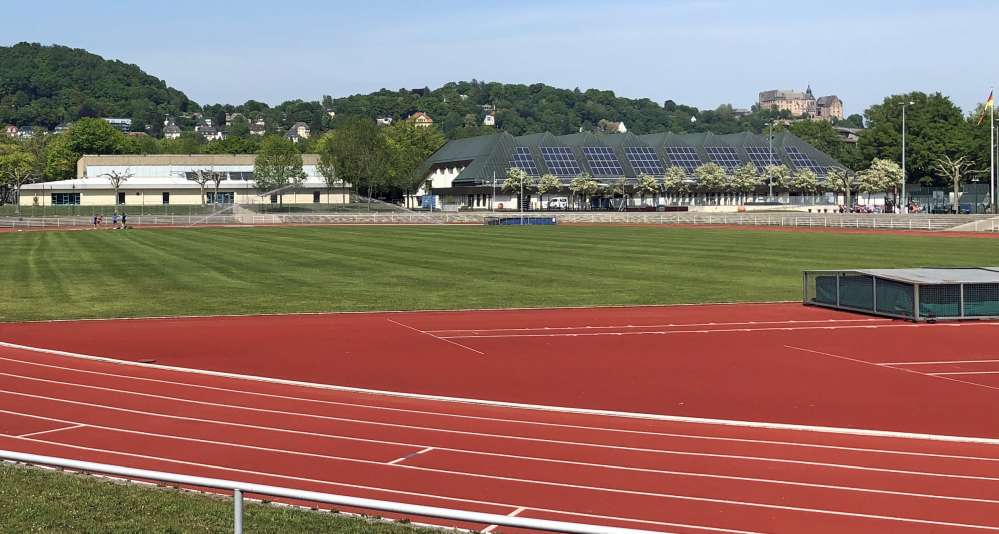 Sportstadion. Dahinter Gebäude und oben am Berg das marburger Schloss