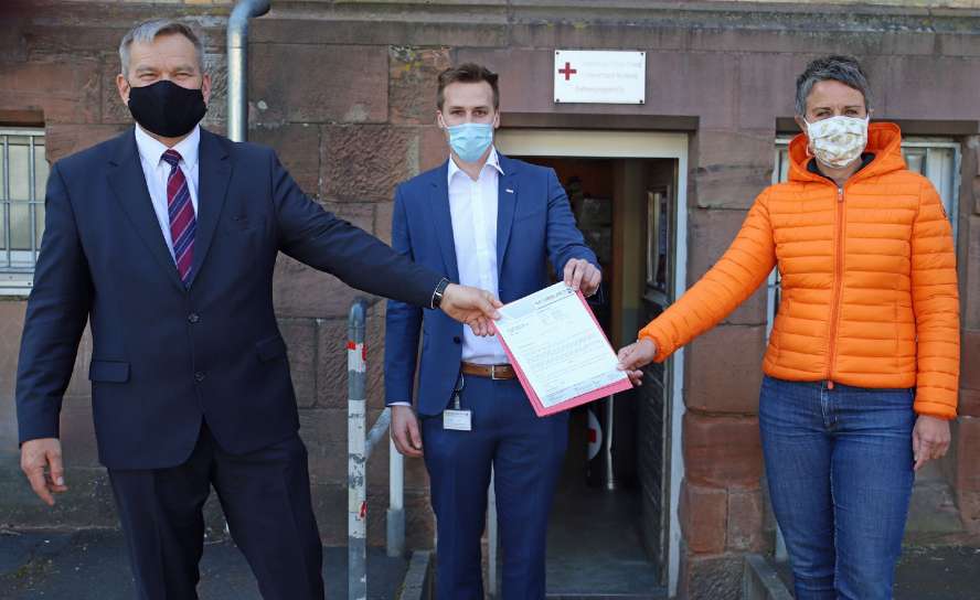 Zwei Männer und eine Frau mit Mund-Nase-Bedeckungen halten zu dritt einen Bescheid.