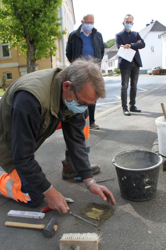 Ein Arbeiter fügt den Stolperstein in den Gehweg ein.
