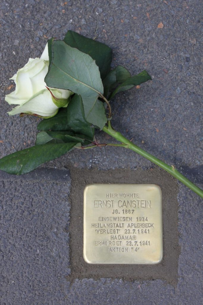 Stolperstein mit Inschrift und eine weiße Rose darüber