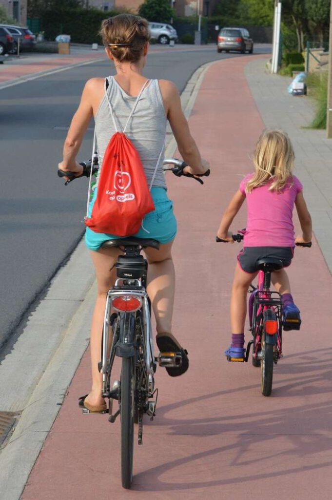 Mutter und Tochter (von hinten) auf einem Radweg radelnd.