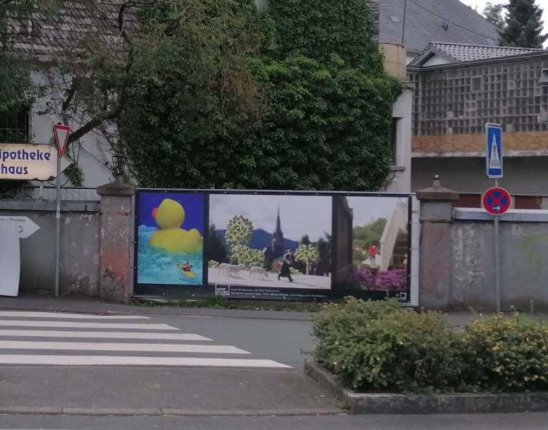 Drei Bilder zieren eine Mauer vor einem Zebrastreifen