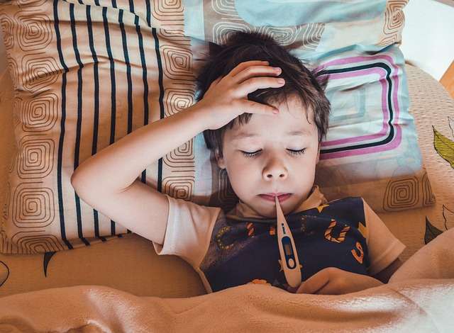 Krankes Kind mit Fieberthermomenter im Mund, liegt im Bett.