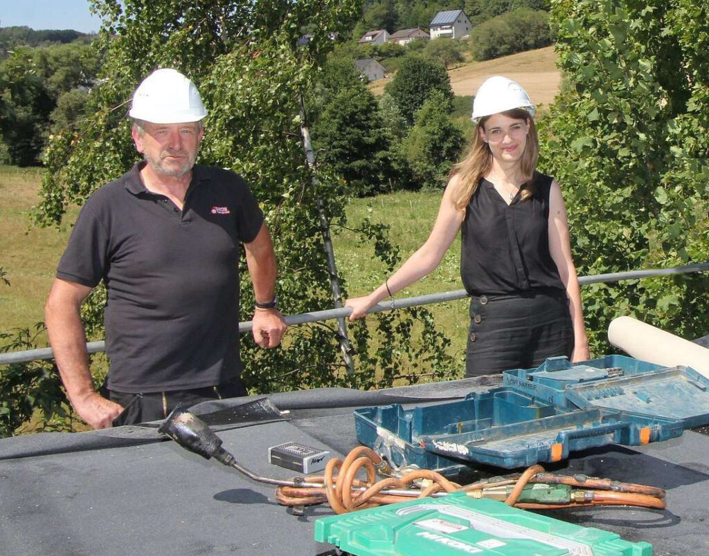 2 Leute mit Bauhelm und Baumaterial am Dach