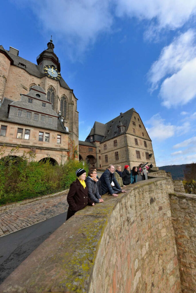 Marburger Schloss und 8 Leute davor an der Mauer.