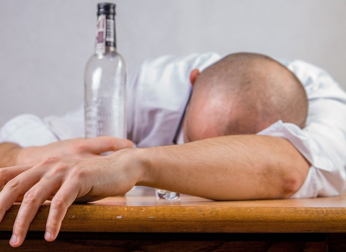 Betrunkener Mann mit leerer Wodkaflasche liegt über den Tisch gebeugt