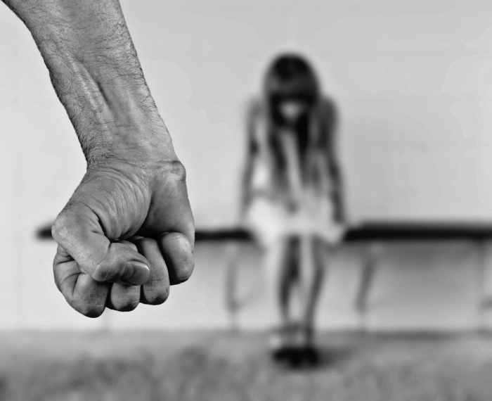Männliche Faust bedroht sitzende Frau in hilfloser Pose