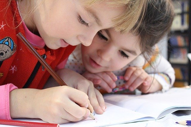 2 Kinder schreiben und stecken die Köpfe zusammen