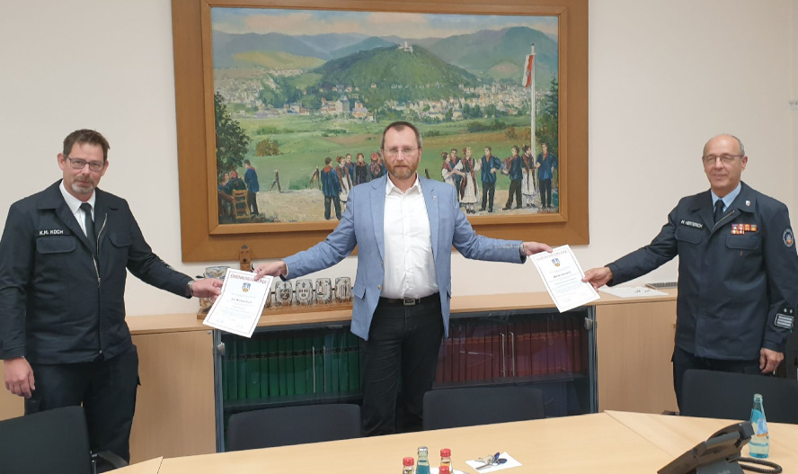 3 Männer die sich die Hände entgegenreichen und jeweils eine Urkunde miteinander halten.
