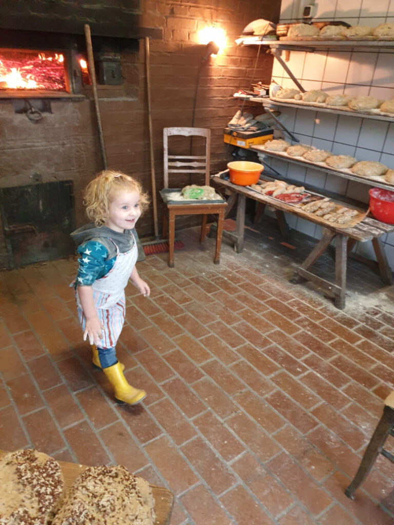 Kleines Mädchen mit Schürze im Backhaus. Feuer im Ofen.
