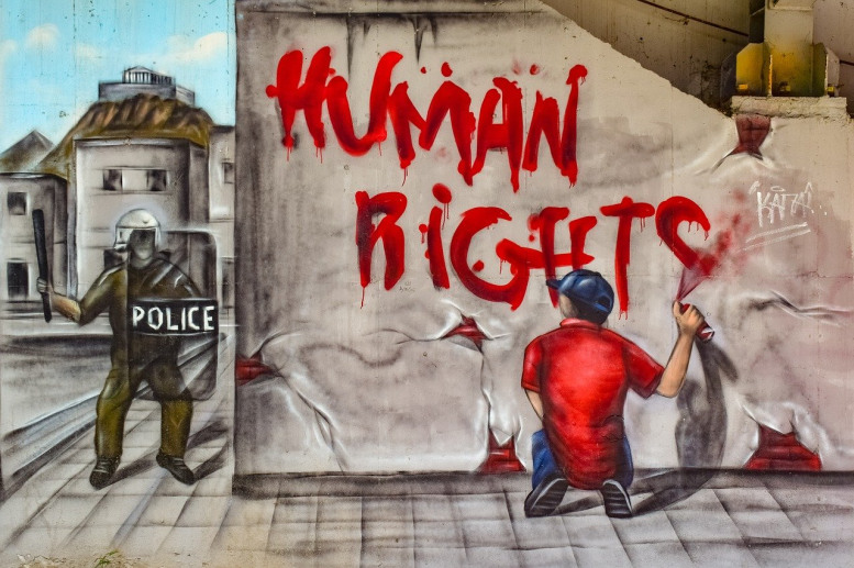 Mann sprüht "Human Rights" an eine Hauswand