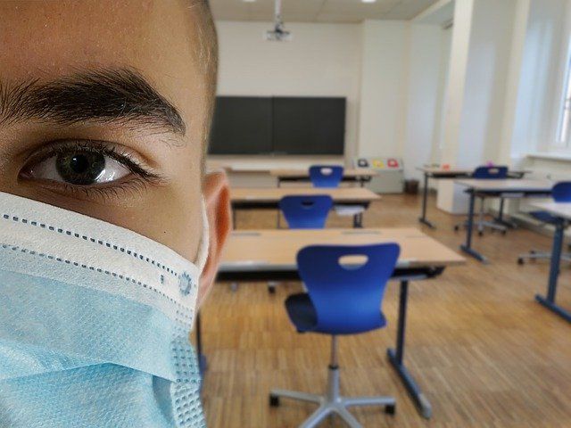 Maskierter Schüler in leerem Klassenraum