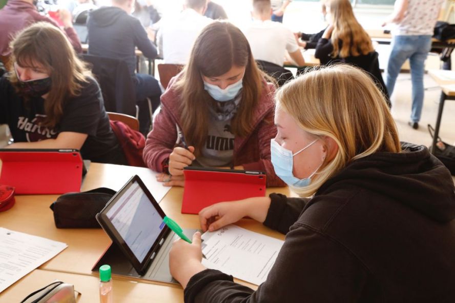 Schülerinnen mit Masken sitzen am iPad und arbeiten.