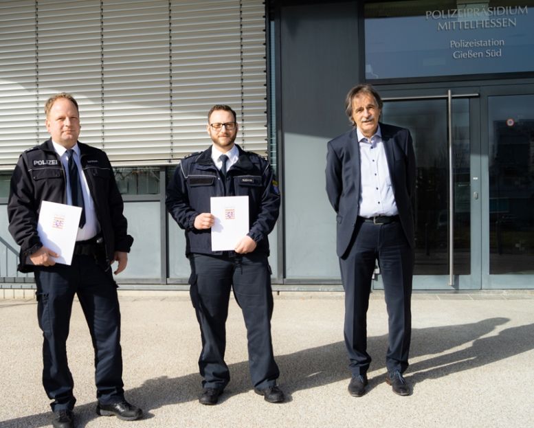 2 Polizisten mit Urkunden und ein Anzugträger vor dem Präsidium